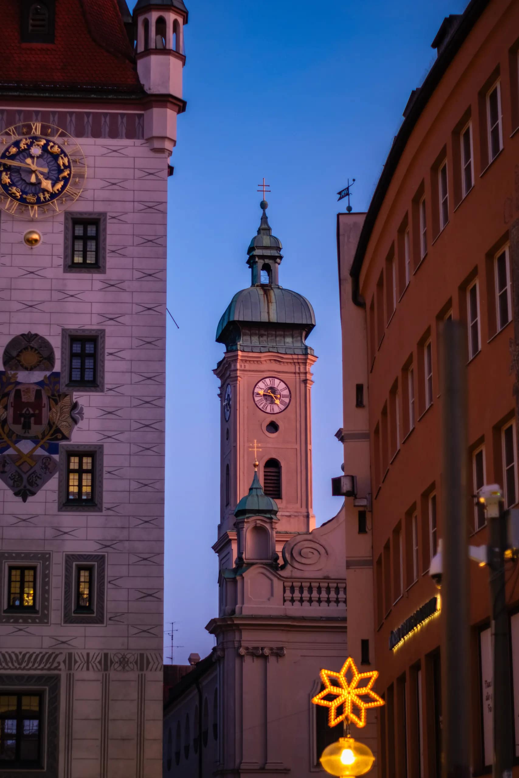 Historic clock towers framed between buildings beneath a deep blue evening sky