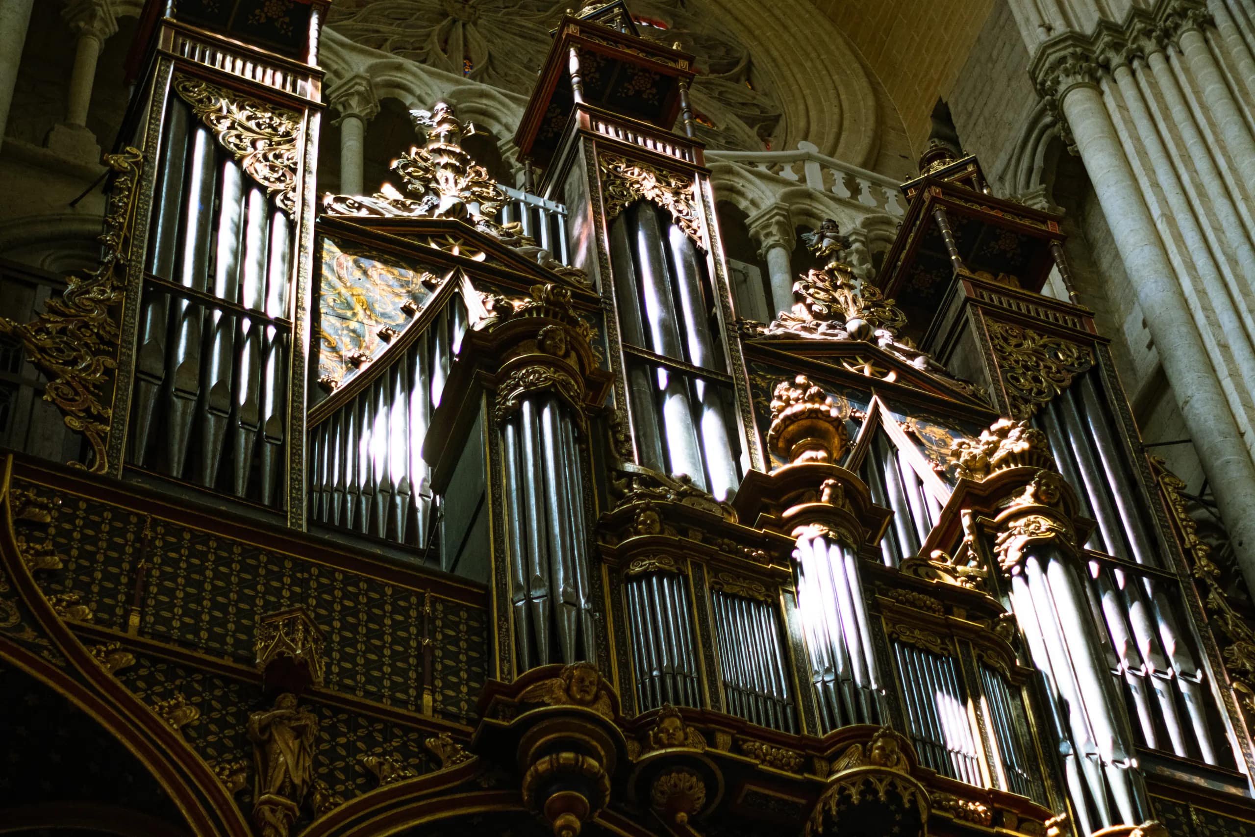 An ornate cathedral pipe organ illuminated inside a vaulted stone interior