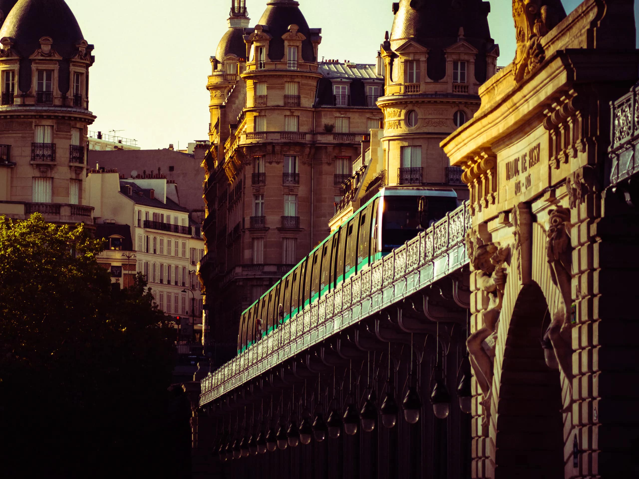 A metro train crossing an elevated Parisian bridge in golden light