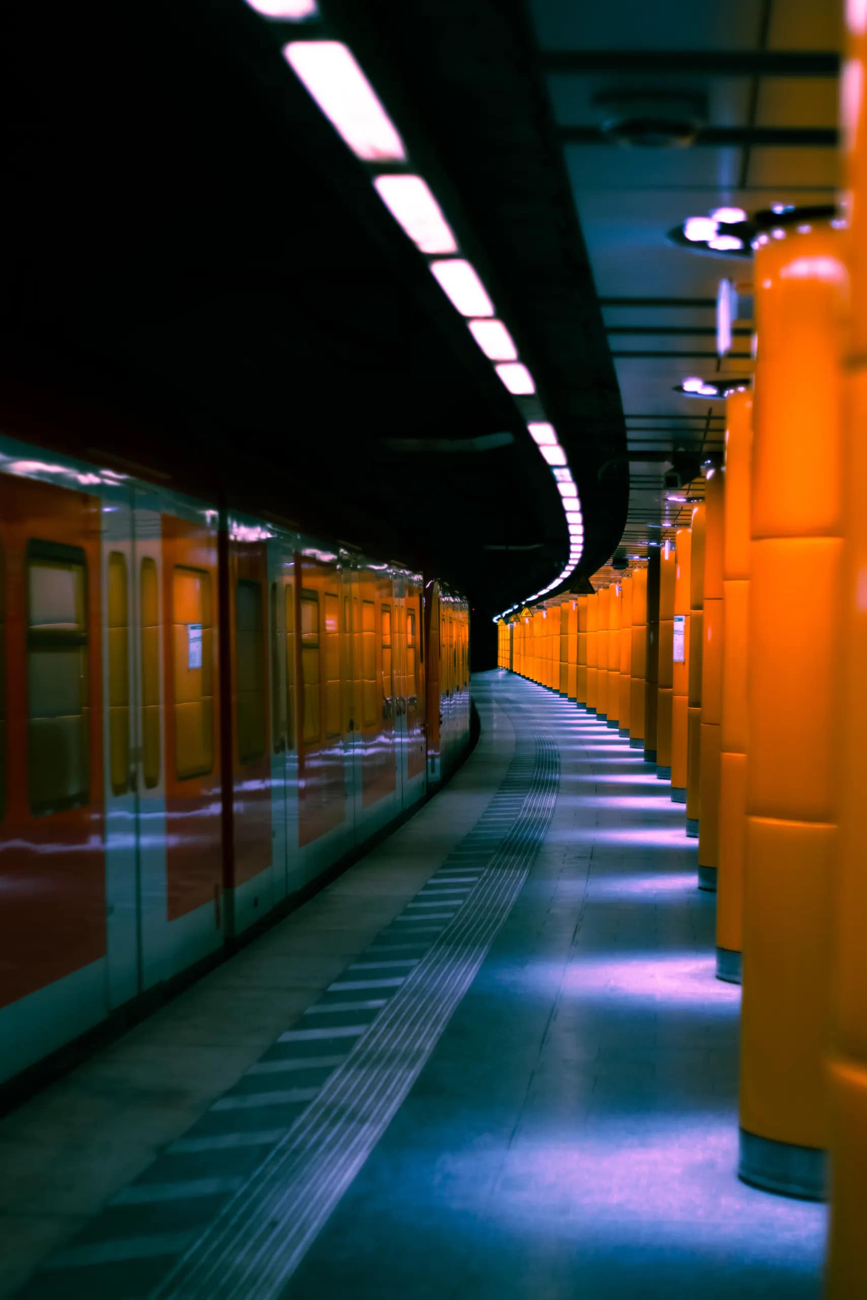 A curved underground station with an orange train and glowing platform lights